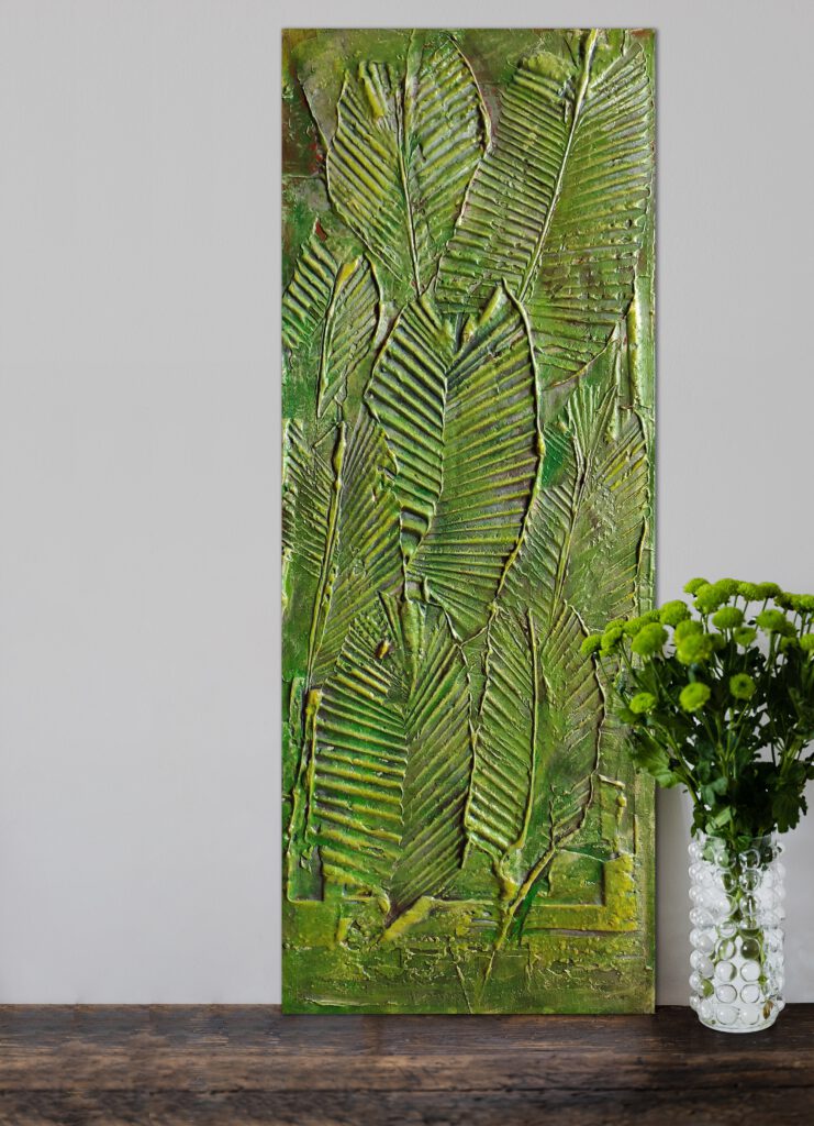 The leaf painting standing on the ground next to a vase of green flowers.