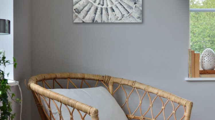 The painting of the shell hanging on a wall, in the corner of a room. The paintings colours pair well with the grey and wood-tones in the room.