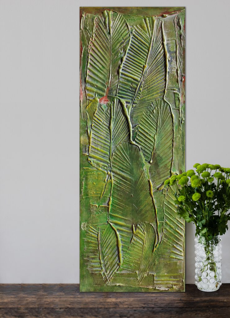 The green leaf painting standing on the wooden floor, next to a flower vase.