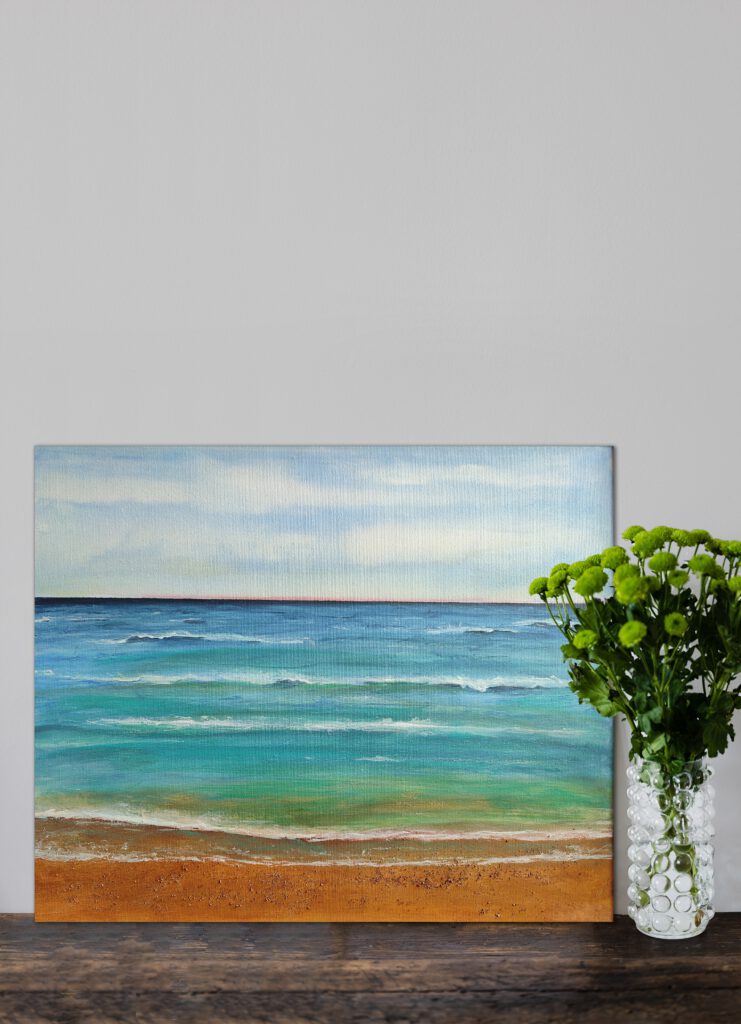 The beach painting standing on wooden floor, next to a flower vase.