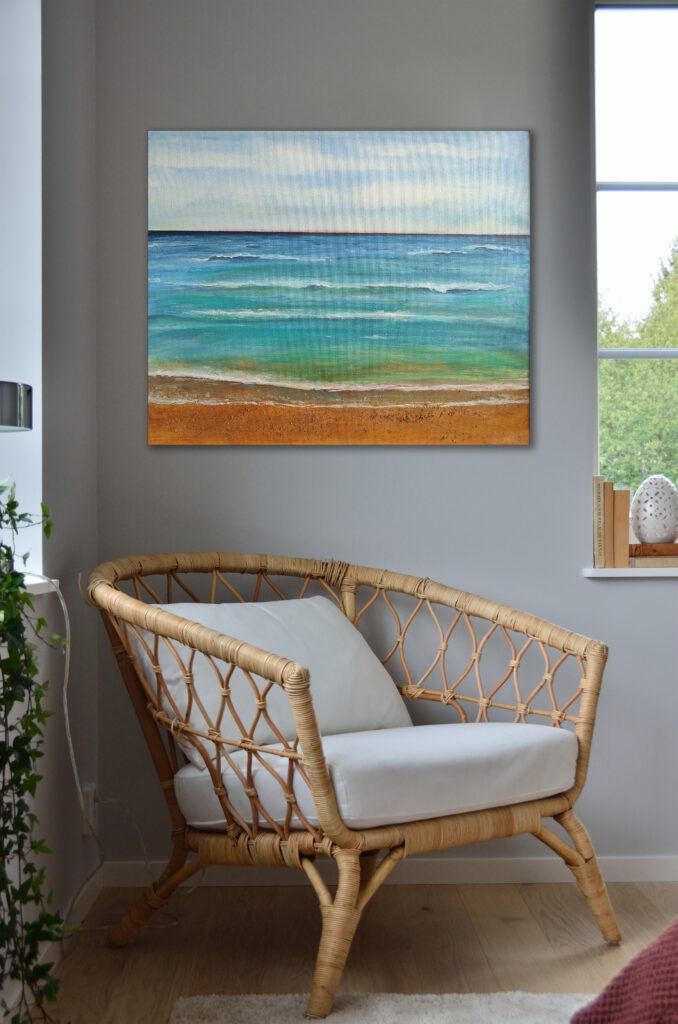 The painting of a beach hanging on the wall of the corner of a grey room.