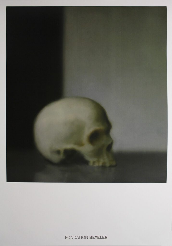 Een schilderij van een schedel zonder kaak; staand in een donkere hoek. Getekend door Gerhard Richter.